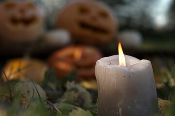 Burning Candle Close Up on Blurred Halloween Pumpkins Heads Background. Pumpkin with Carved Scary Smiling Face Outside. Jack-O-Lantern Outdoors. Halloween Composition Backyard Decor. All Saints Day 4K