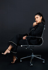 Portrait isolated cutout studio shot Asian female glamour elegant powerful fashion businesswoman model in black casual fashionable suit and high heels sitting crossed legs posing on dark background