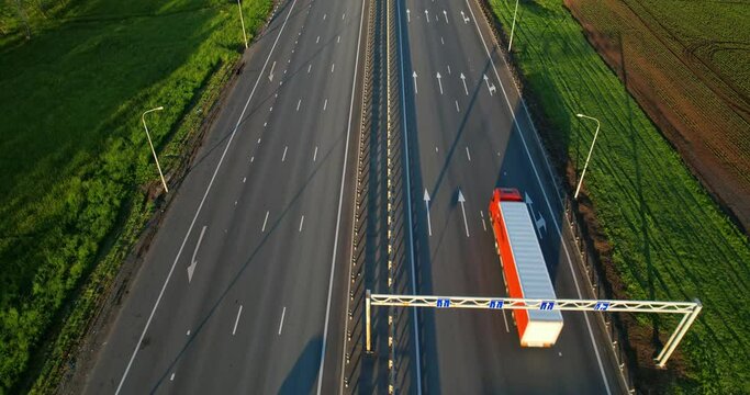 Traffic of cars and trucks on a six-lane highway on a summer day, aerial view. A multi-lane road. Trucks with trailers are driving along the highway one after another. Road markings.