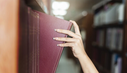 A white woman's hand picked up a book from a shelf in the library.
