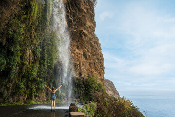 Cascata dos Anjos - woman standing under Angels waterfall in Madeira - obrazy, fototapety, plakaty