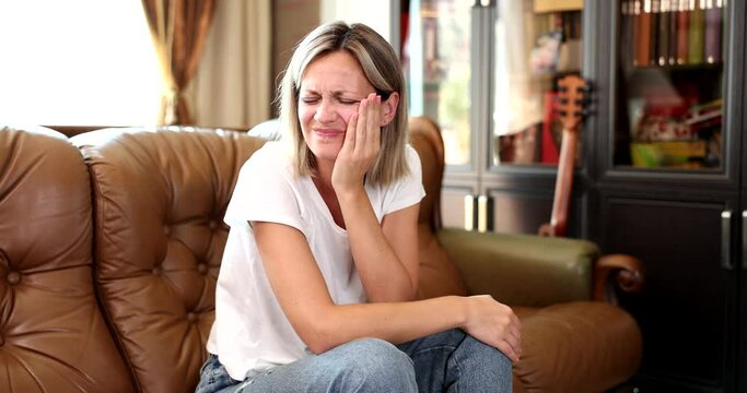 Woman suffering from toothache touches face sitting on sofa at home