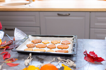 Cookies for Halloween baked in the oven cool on a baking sheet. The table will be decorated with leaves, a toy skeleton and pumpkins.