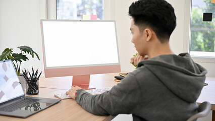 Smart young Asian male programmer or office worker working at his desk, using PC computer