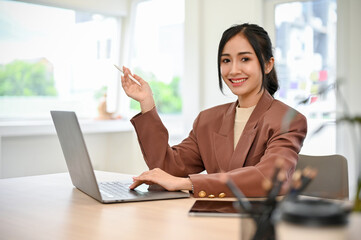 Beautiful Asian businesswoman working at her desk, smiling and looking at camera.