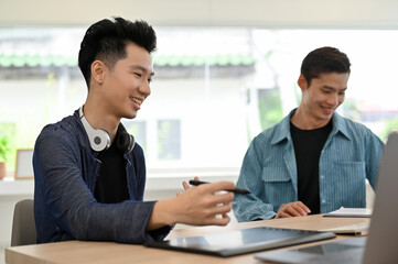 Two smart millennial Asian male web developers discussing and working together