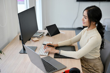 Charming Asian female web developer or graphic designer working at her desk.