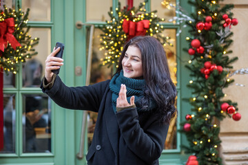 Happy woman using smart phone in city with background of festive Christmas decoration.