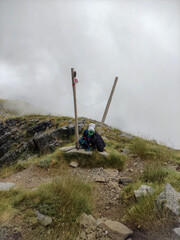 Hiking sign pointing the hiking trail path at cloudy mountain above the clouds
