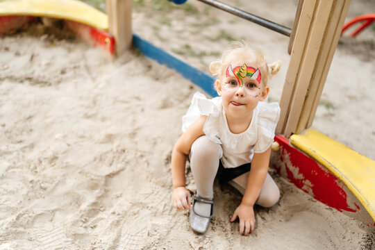 child with a unicorn mask on his face plays in the sandbox outside in the summer.