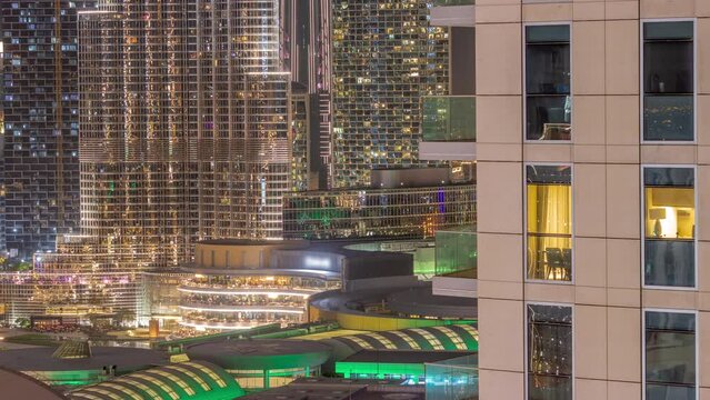 Shopping Mall Exterior During Earth Hour With Reastaurants On Balconies Night Timelapse In Dubai, United Arab Emirates. Aerial Top View With Tallest Skyscraper On A Background. Lights Turning On