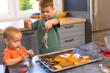 The boy plays with his brother in the kitchen and holds a toy skeleton in his hands. The child is in the kitchen helping to bake and decorate Halloween cookies.