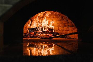 A traditional oven for cooking and baking pizza with a shovel. Firewood burning in the oven. Wood-fired oven. Image of a brick pizza oven with fire.