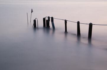 Old damaged concrete and metal pier partially submerged with a silky  smooth sea.  Long exposure photograph.
