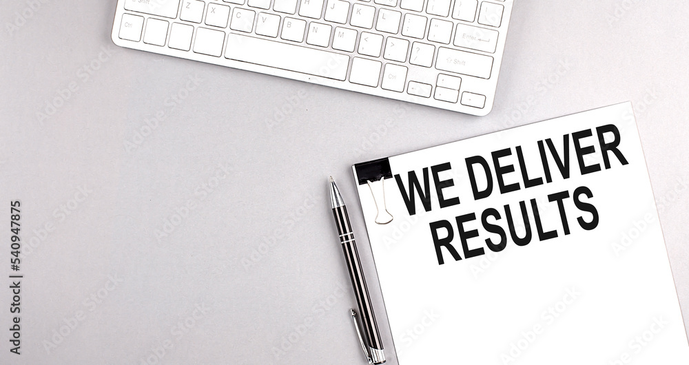 Aufkleber we deliver results text on paper with keyboard on grey background