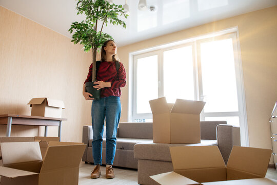 А Woman With A Flower In Her Hands Stands In Her New Apartment. The Concept Of Moving To A New Place Of Residence Or Moving Out Of An Old Home