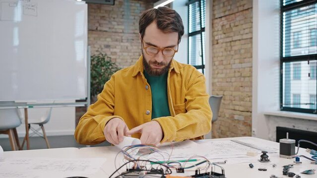 Young man in glasses rolls paper scheme of device prototype