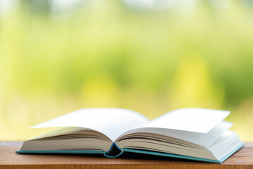 Open book on wooden table on natural background. Concept of reading books. Wind turns the pages. Image with shallow depth of field.