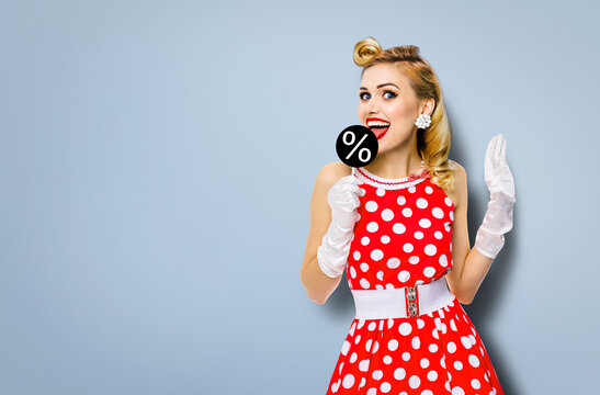 Very tasty discounts, rebates, deals concept image. Cheerful beautiful woman licking signboard with % sign, dressed in pinup red dress, isolated over grey background. Black Friday sales ad.