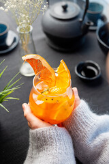 Warming orange drink with cloves. A woman holds an aromatic glass in her hands