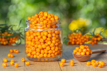 Sea buckthorn berries in a glass jar on a wooden table