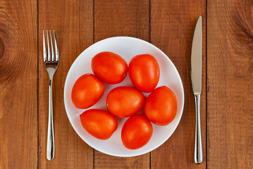Red tomatos on a white plate. A plate with vegetables on the table. Diet food. Vegetarian food.