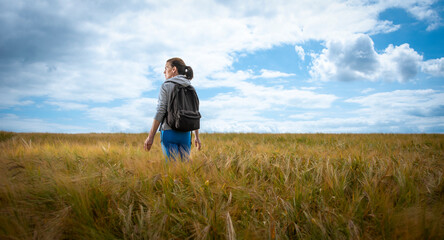 Naklejka na ściany i meble Woman with a backpack walking through a field, enjoying the countryside.