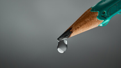 Tip of a pencil with a drop on gray background