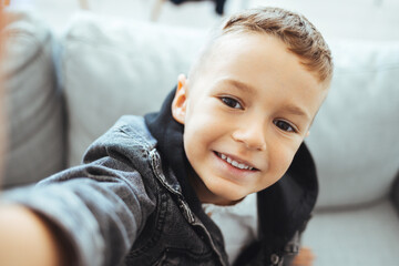 Cute little boy taking selfie on light background. Happy little boy with healthy teeth taking...