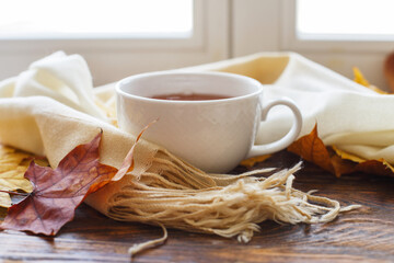 autumn leaves with a cup of tea or coffee next to a scarf on a wooden background with copy space