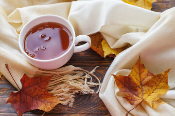 autumn leaves with a cup of tea or coffee next to a scarf on a wooden background with copy space
