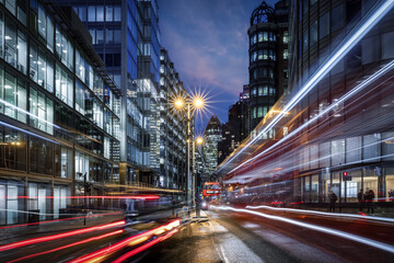 Fototapeta na wymiar Evening view of a busy road in the City of London with traffic light trails and illuminated skyscrapers in the background, England