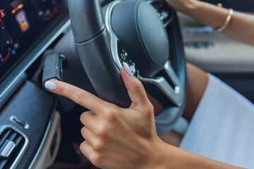 Woman's hand switches the lobes of the gear selector on the steering wheel. Hand is switching car gear lever, close up shot of a manual gear changing paddle on a car's steering wheel.