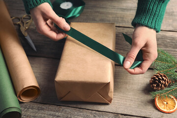 Christmas present. Woman tying ribbon around gift box at wooden table, closeup