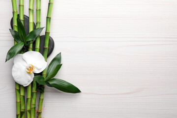 Spa stones, bamboo and orchid flower on light wooden table, flat lay. Space for text