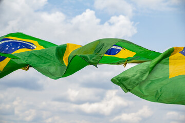 Algumas bandeiras do Brasil balançando ao vento com o céu nublado ao fundo. - obrazy, fototapety, plakaty