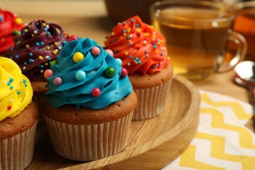 Delicious cupcakes with colorful cream and sprinkles on wooden board, closeup