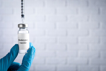 Nurse filling syringe with monkeypox vaccine from vial near white brick wall, closeup. Space for...
