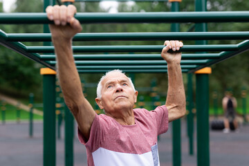 Obraz premium Active grandfather moves with the help of his hands on a horizontal ladder on sports ground