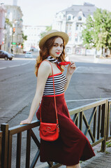 Fashion portrait of young, happy, elegant redhead curly woman, girl in hat and casual clothes. French style. Walking, relax in the city street. Sunny day.