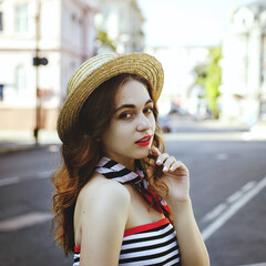 Fashion portrait of young, happy, elegant redhead curly woman, girl in hat and casual clothes. French style. Walking, relax in the city street. Sunny day.