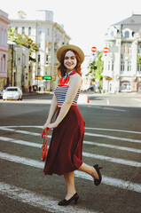 Fashion portrait of young, happy, elegant redhead curly woman, girl in hat and casual clothes. French style. Walking, relax in the city street. Sunny day.