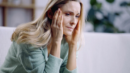 sad woman having migraine while touching head in living room