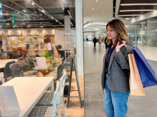 Young Caucasian attractive woman standing indoor in shopping mall looking at showcase with home furniture. Pretty female choosing table and chairs. Furniture for dining room