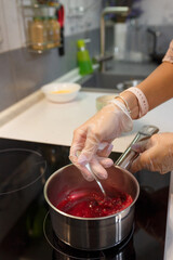 Obraz na płótnie Canvas Making jam. Hands in gloves mixing sugar and berries with spoon in saucepot on stove. Seasonal berry jelly or marmalade. Kitchen background