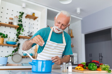 Happy senior man having fun cooking at home - Elderly person preparing health lunch in modern...