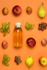 Bottle With Apple Cider or Vinegar with Raw Autumn Fruits Grape Apples Pears Plums on Orange Background Top View Vertical