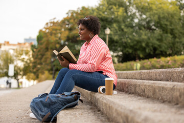 Obraz premium Curvy afro woman reading book outdoors
