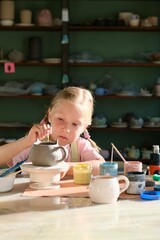 A little girl makes a cup out of clay in a pottery workshop. The concept of children's creativity. Child pottery making