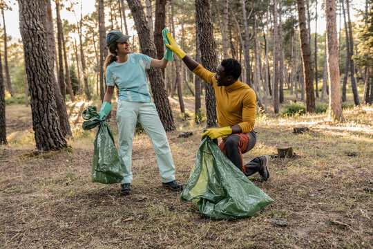 Two diverse volunteers giving each other high five after they cleaned the area of the garbage - Powered by Adobe